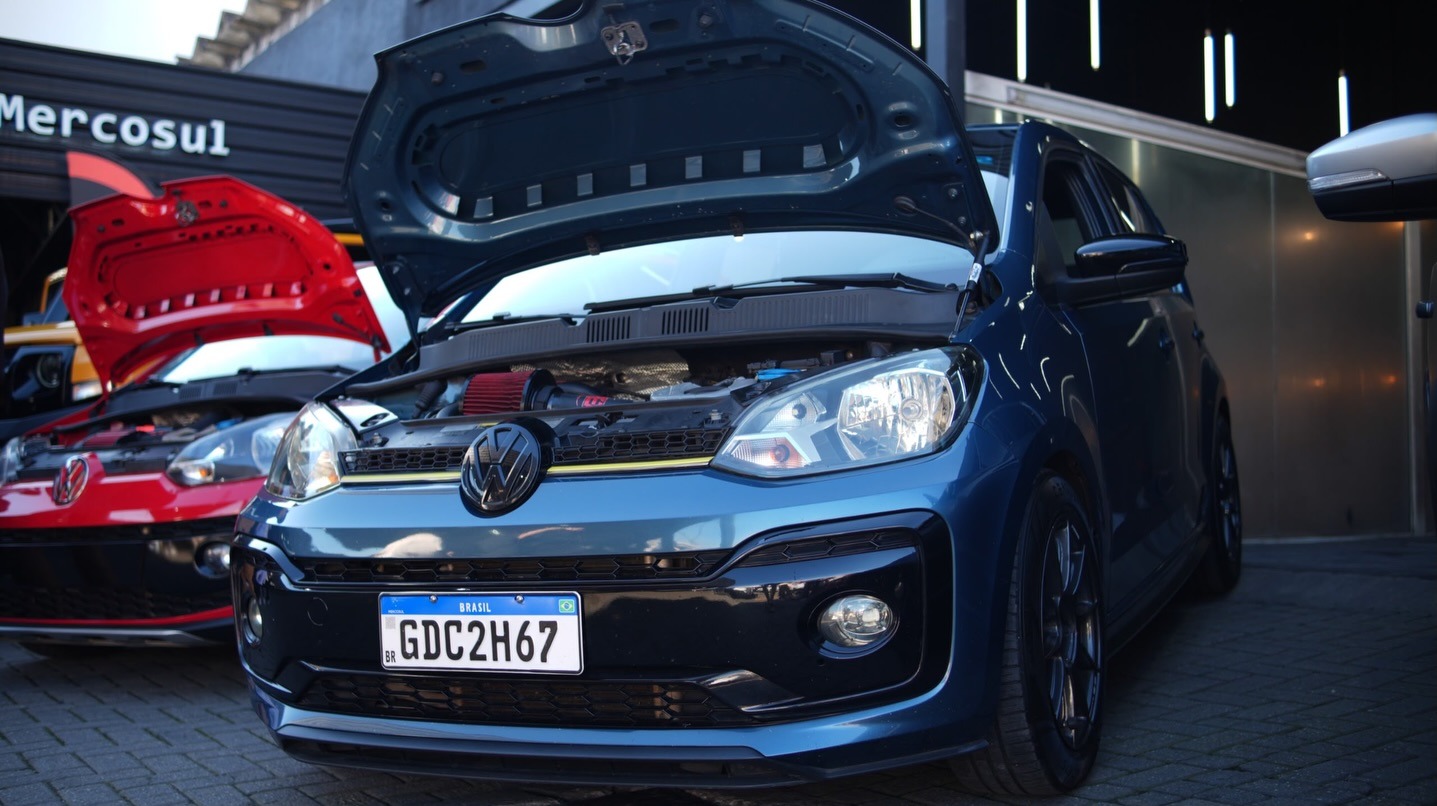 VW Up! com capô aberto em oficina premium ao lado de outro veículo